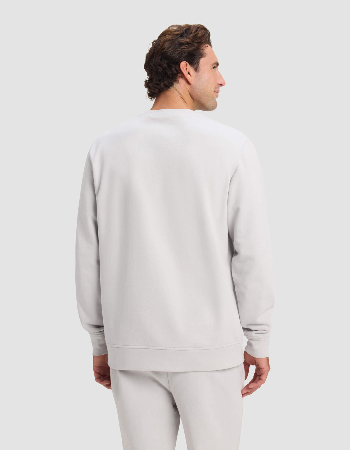 A man with short brown hair is seen from the back, wearing Cozy Earth's Men's Dylan Crewneck sweatshirt and matching sweatpants, standing against a light gray background.