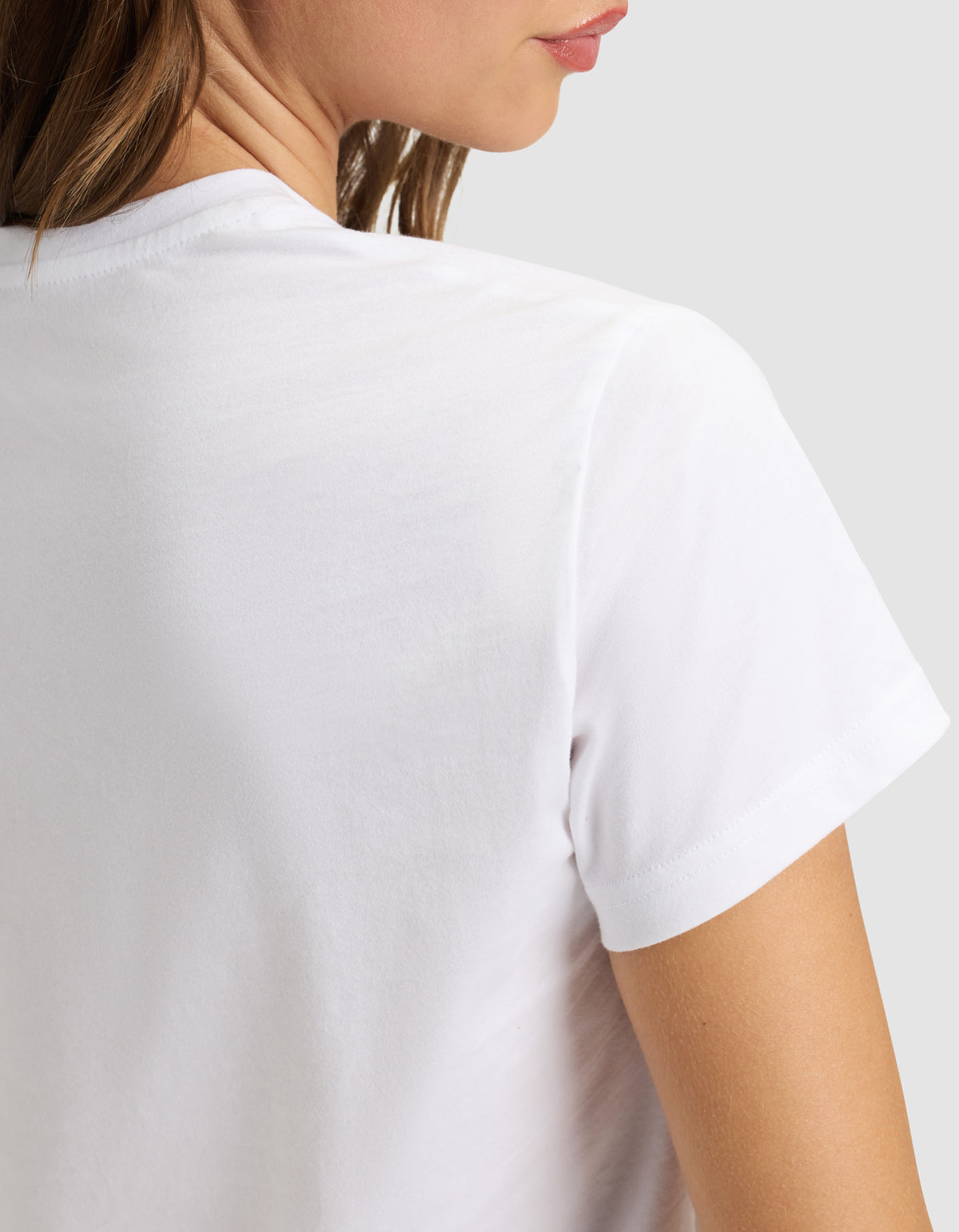 A woman wears the Cozy Earth Women's Easy Tee, shown from the back and slightly to the side, with part of her face, neck, and shoulder visible against a plain light background. 