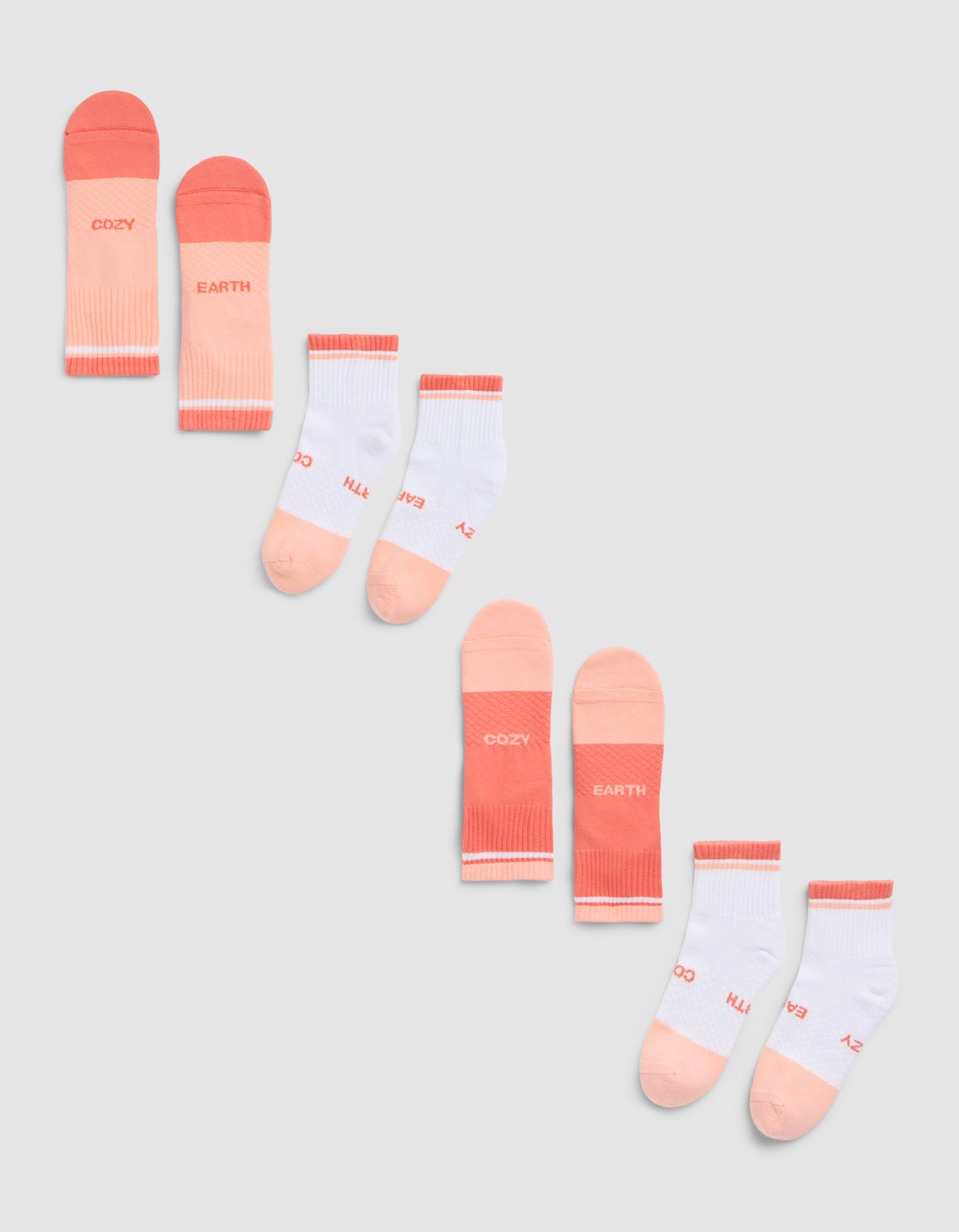 The Cozy Earth Essential Quarter Sock 4-Pack is shown on a gray background, featuring peach and pink pairs with "COZY" and "EARTH" text, plus white pairs accented in peach and pink with similar lettering. |Color:Cantaloupe