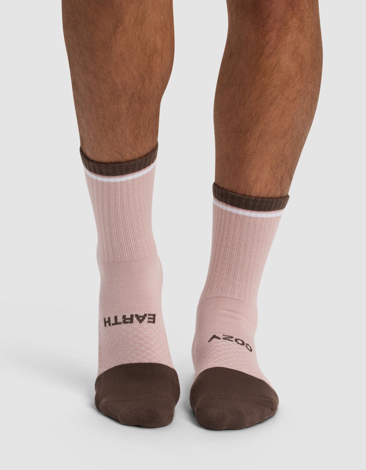 A person wears Cozy Earth's Essential Calf Socks in pink with brown toes and cuffs; "EARTH" is printed in black on the left sock and "COZY" on the right, both across the tops of the feet.