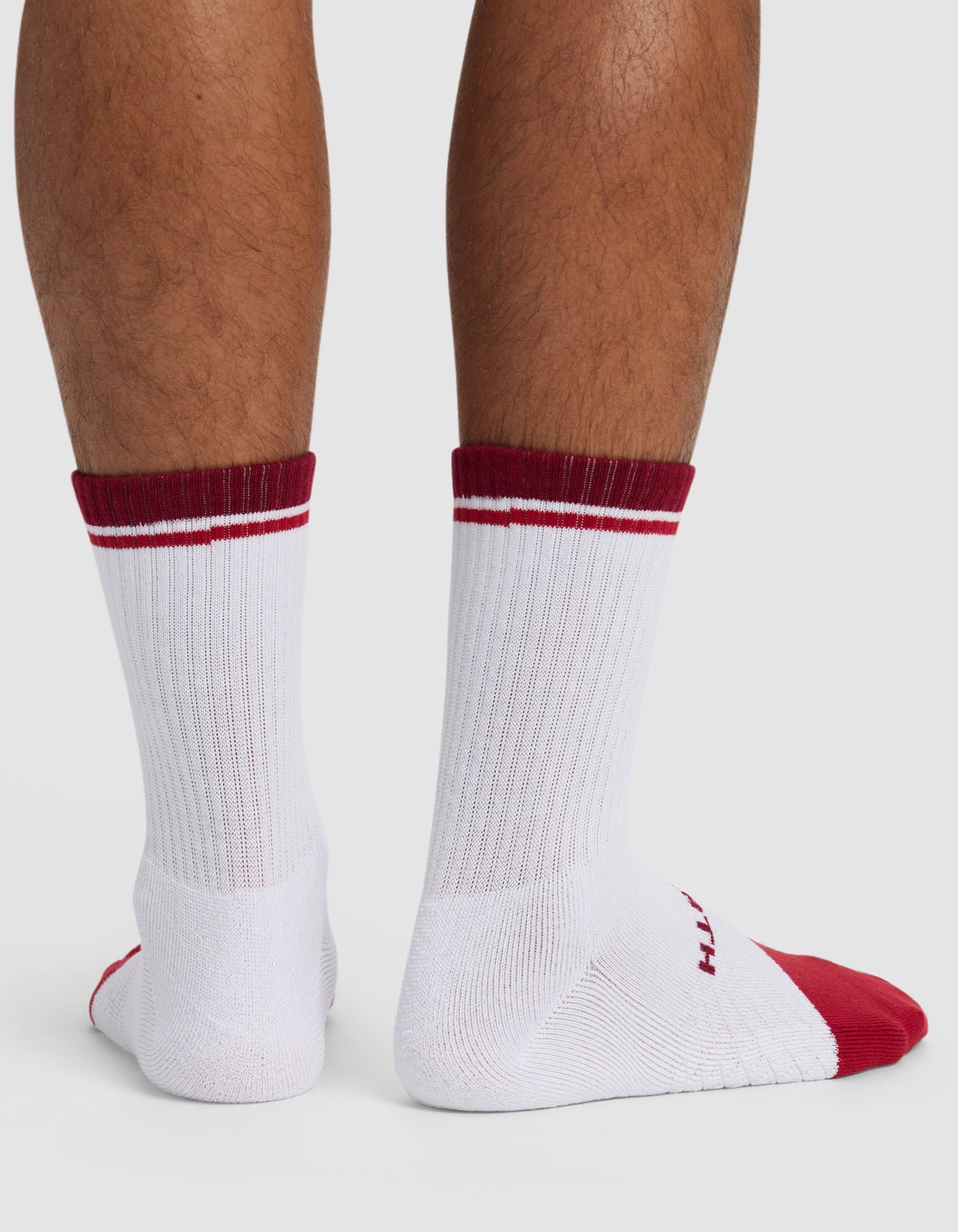 A pair of legs wearing Cozy Earth Essential Calf Socks in white, featuring red toes, heels, and top stripes. These ribbed socks display partially visible text on the soles against a plain white background.