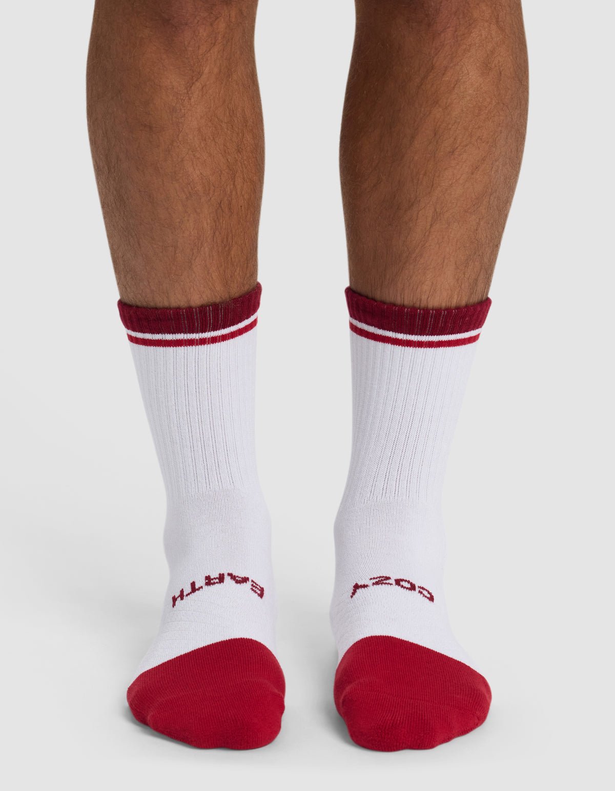 Someone wearing Cozy Earth's Essential Calf Sock in white, featuring red toes, heels, top stripes, and red "EARTH" on the left sock and "COZY" on the right sock near the toes.