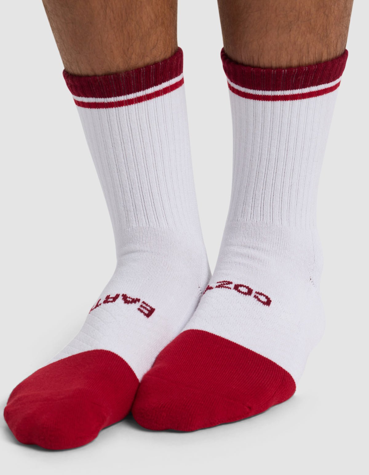 A person wears Cozy Earth's Essential Calf Sock: white crew socks with red toes, heels, cuffs, two red stripes on the cuffs, and red text on the top of the feet.