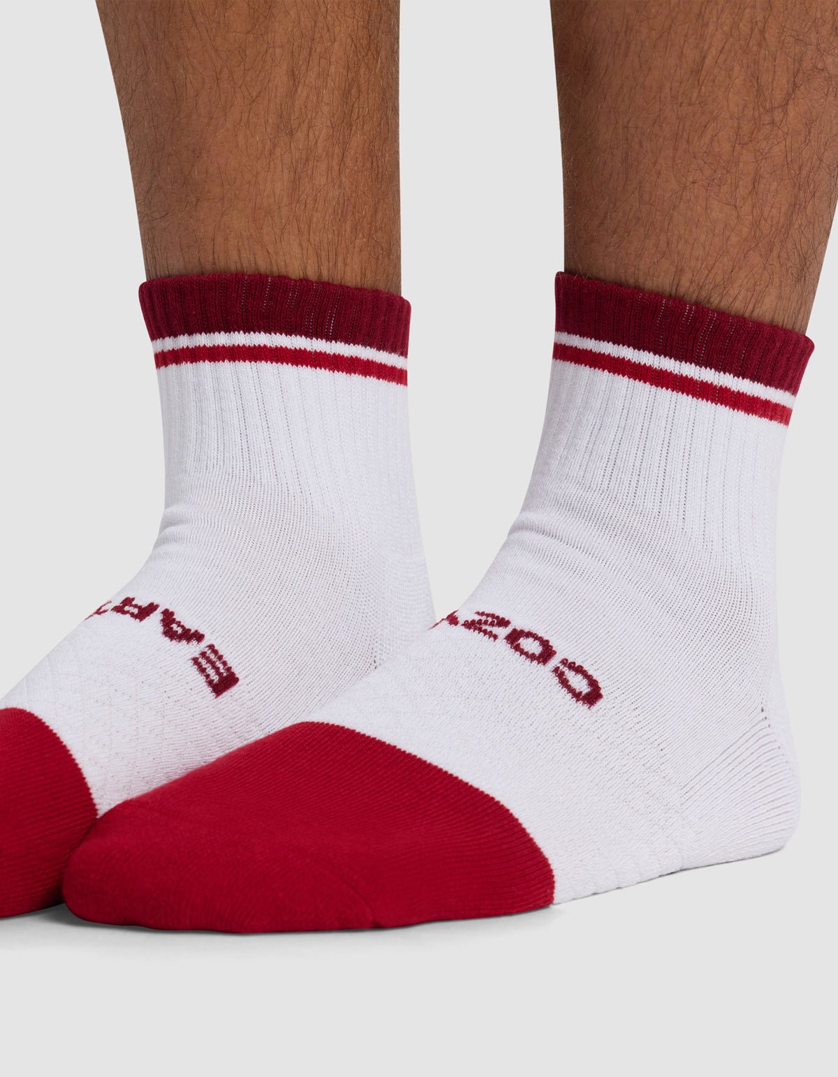 Close-up of feet wearing Cozy Earth Essential Quarter Socks—white with red toes, heels, cuffs, two thin red stripes near the top, and partially visible red text on the upper foot.