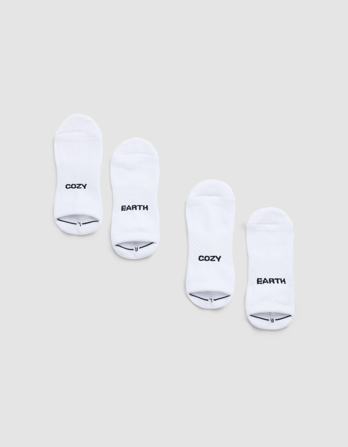 Two pairs of Cozy Earth Essential Ankle Socks are displayed side by side on a light gray background, each featuring black text near the toes—one in each pair reads "COZY" and the other reads "EARTH. 