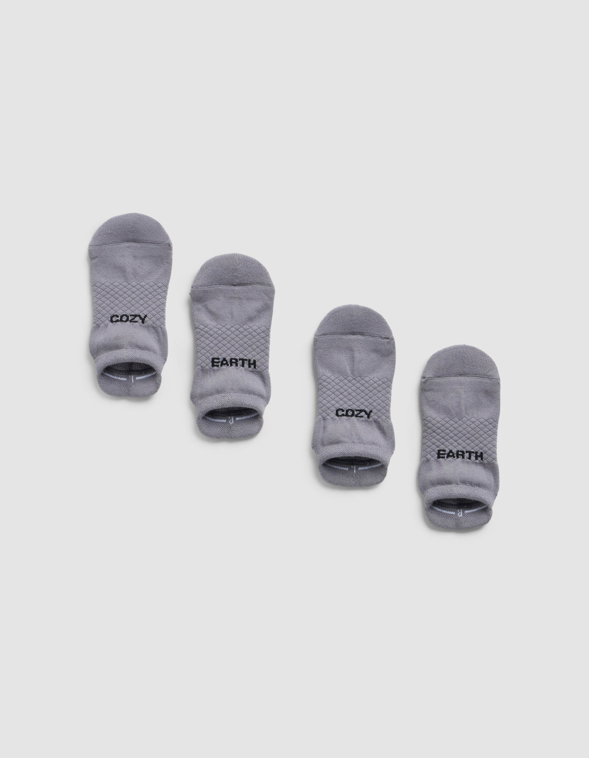 Four small gray Essential Ankle Socks by Cozy Earth are arranged in two pairs on a white background. The left pair has "COZY" and the right pair has "EARTH" printed in black text near the cuff.|Color:Stone