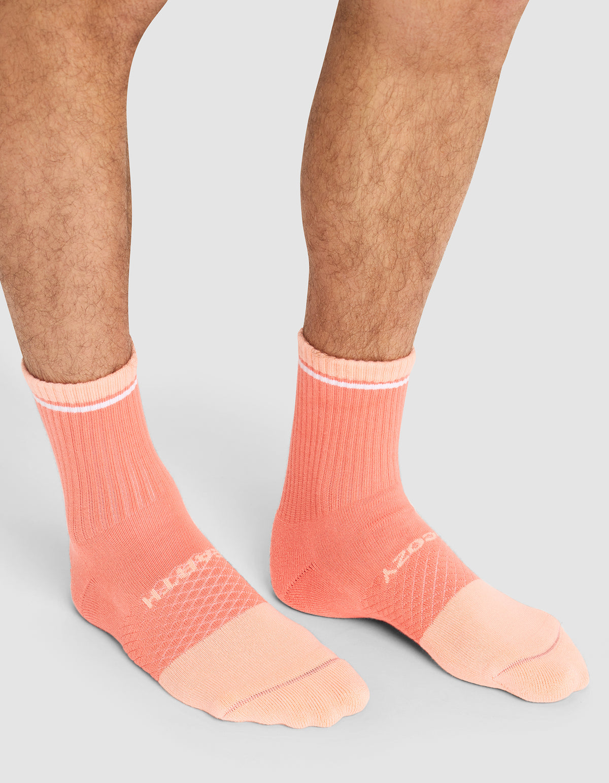 A person wears Cozy Earth Essential Calf Socks in peach with white text and accents, featuring ribbed cuffs and textured panels, standing on a light gray background. Only their lower legs and feet are visible.  