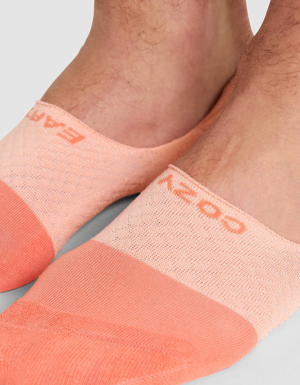 Close-up of two feet wearing Cozy Earth Essential No-Show Socks in peach with textured patterns and "COZY" visible on the top of one sock. 