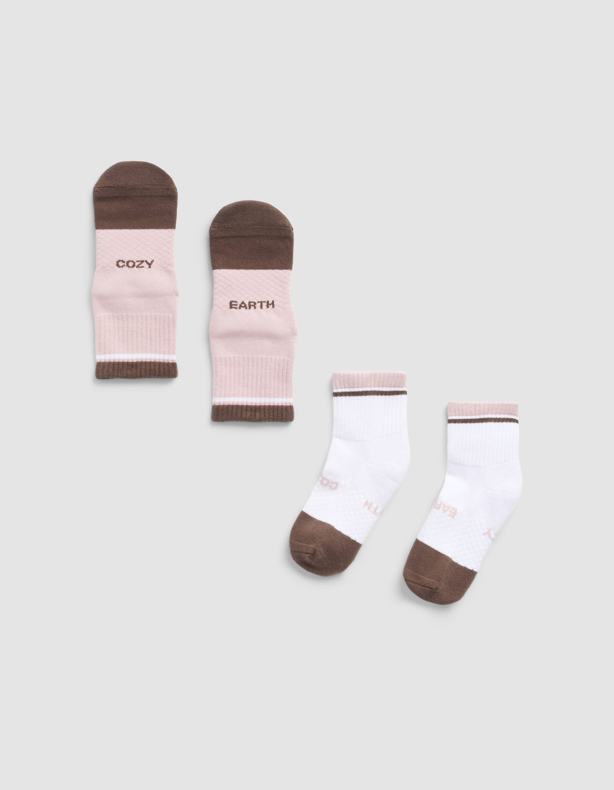 The Cozy Earth Essential Quarter Sock set includes two pairs: one pink and brown pair with "COZY" and "EARTH" text, and one white pair with brown toes, heels, and light pink accents. All are shown on a light grey background.