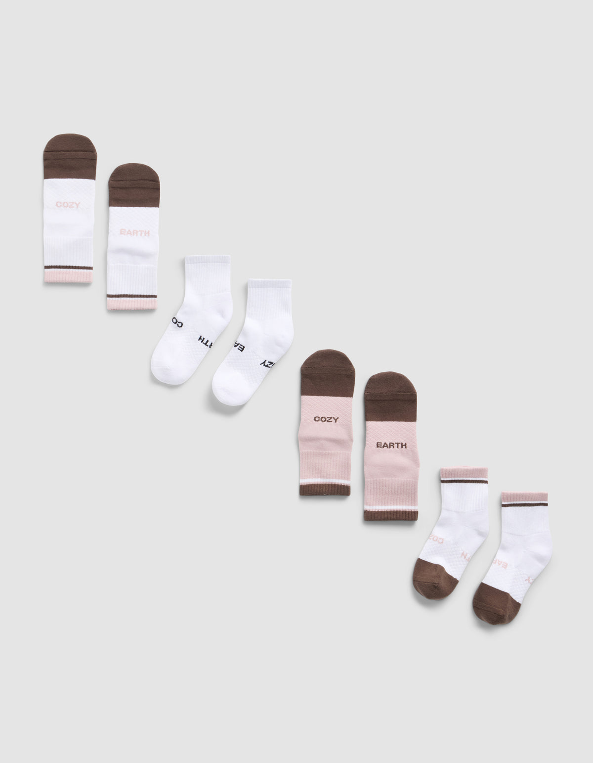 A diagonal row of six pairs of Essential Quarter Sock 4-Packs by Cozy Earth in brown, white, and pink on a light gray background. Some socks feature printed text like "COZY," "EARTH," 