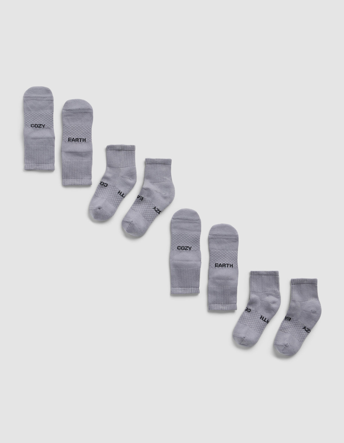 Four pairs of light gray Essential Quarter Socks by Cozy Earth are arranged diagonally on a white background, each pair featuring different words like "COZY," "EARTH," printed in black near the toes.
