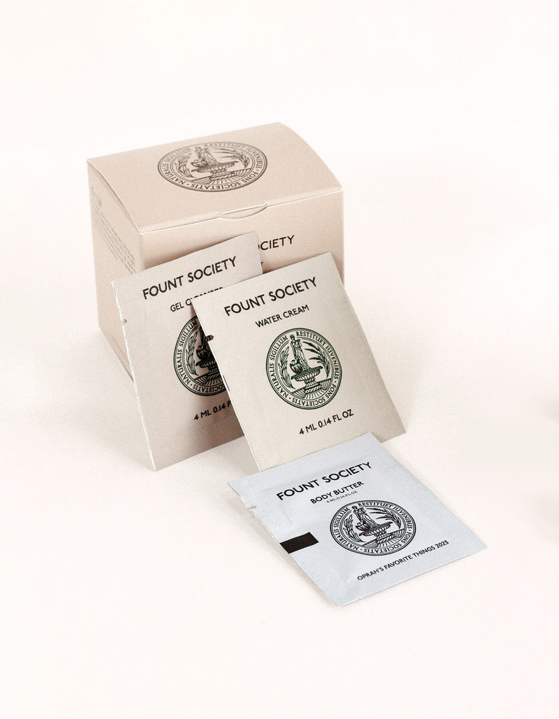 Three sample sachets from the Fount Society Intro Kit by Cozy Earth—Gel Cleanser, Water Cream, and Body Butter—are displayed in front of a beige product box.