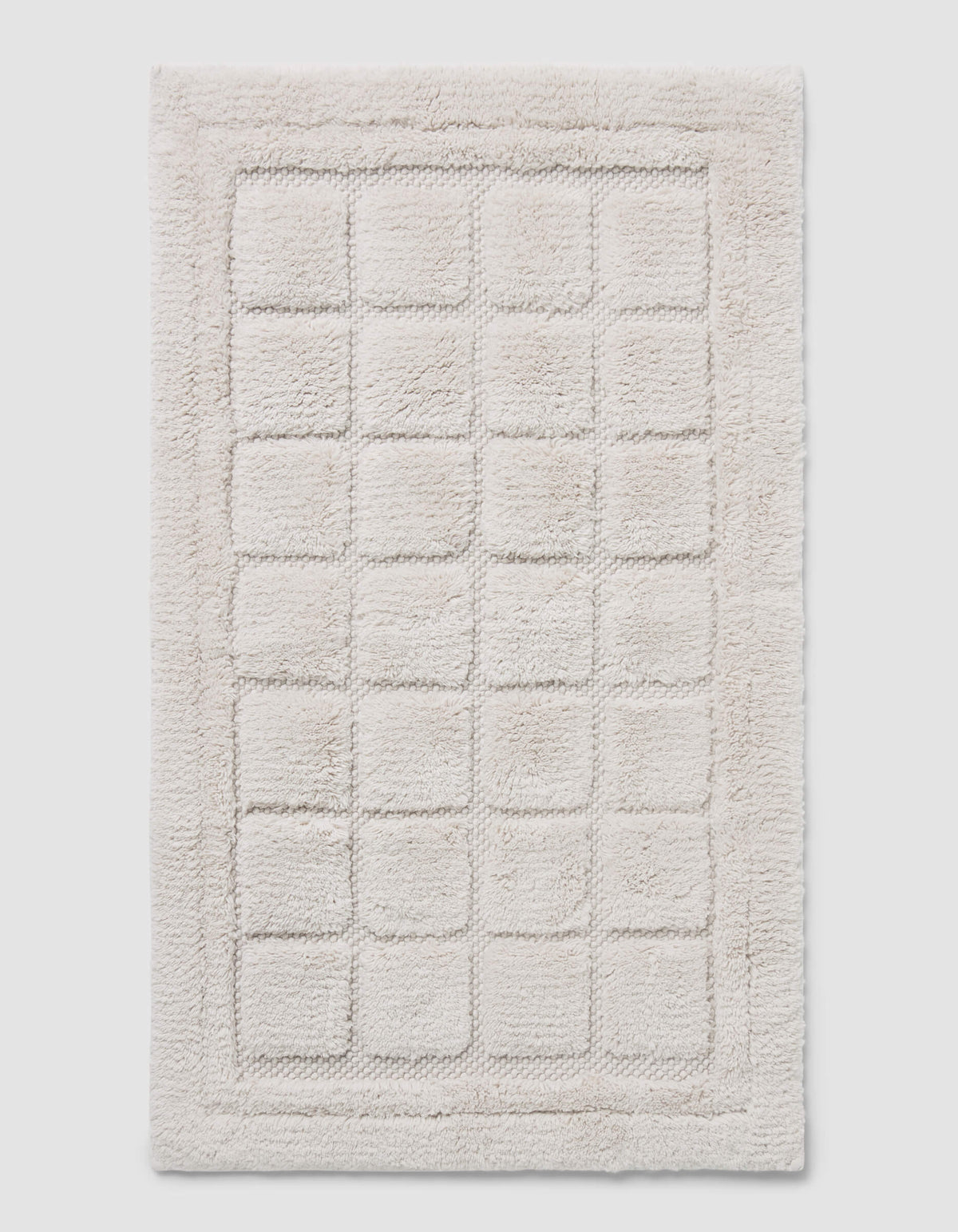 The Cozy Earth Grid Bath Mat is a rectangular, off-white mat with a raised grid design and a thick, fluffy border.|Color:Light Grey