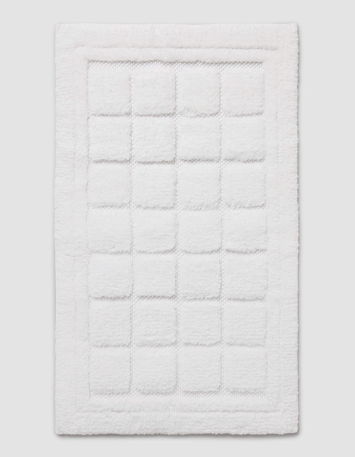 The Cozy Earth Grid Bath Mat is a white, rectangular mat featuring a textured square pattern in the center and a raised border around the edge, shown on a plain background.