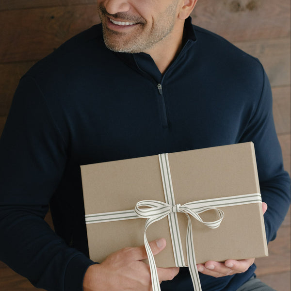 Man holding a gift box with a ribbon in a wooden interior setting.