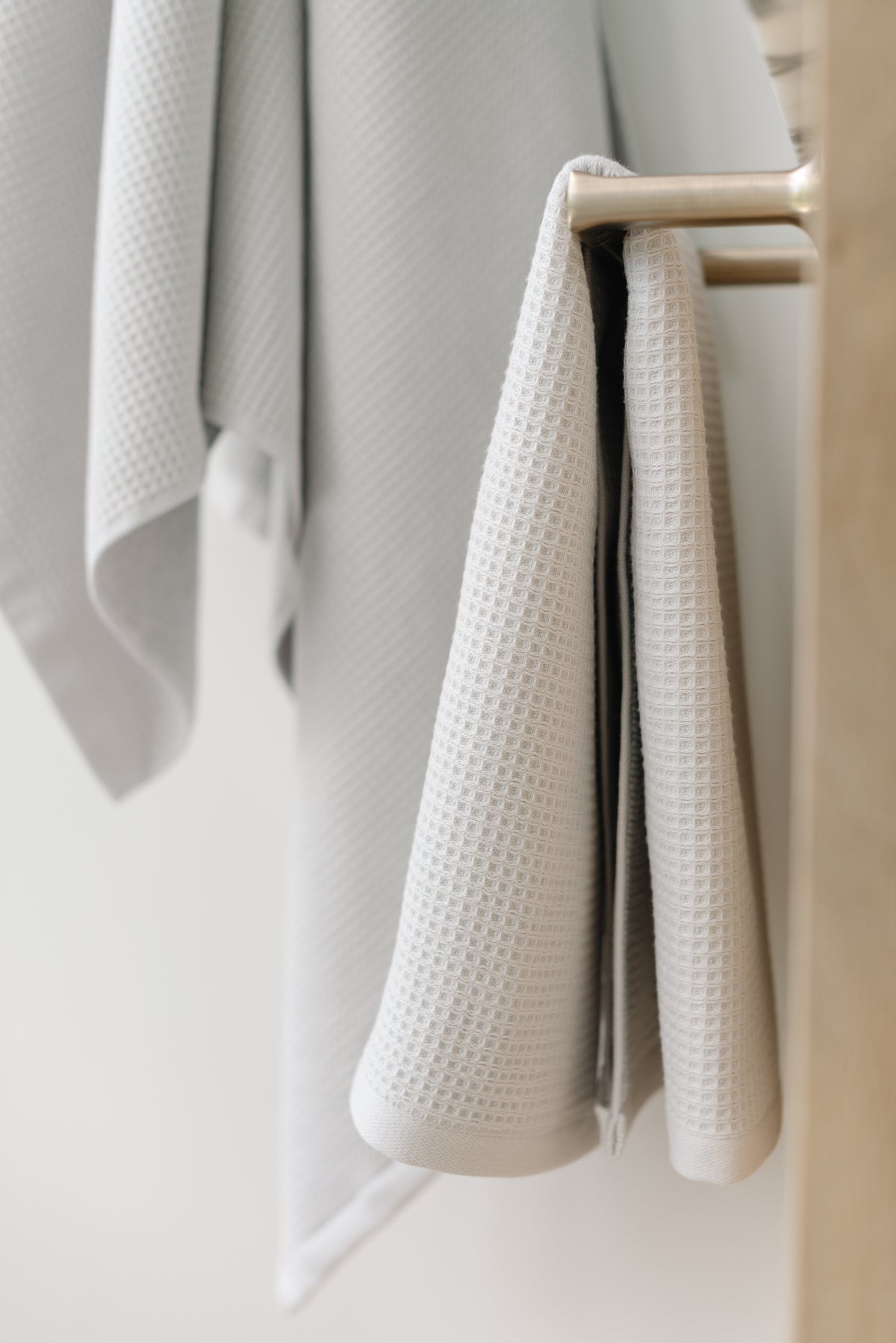 Waffle Hand Towel in the color Light Grey. Photo of Light Grey Waffle Hand Towel taken with the Light Grey Waffle Hand Towel hung from a towel ring. The picture was taken in a bathroom. 