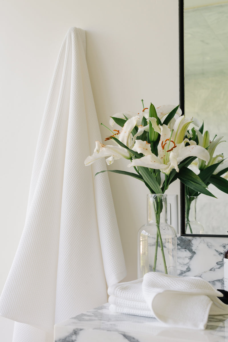 Waffle Bath Towel in the color White. Photo of White Waffle Bath Towel taken as the Waffle Bath Towel hangs from a bathroom wall from a towel.