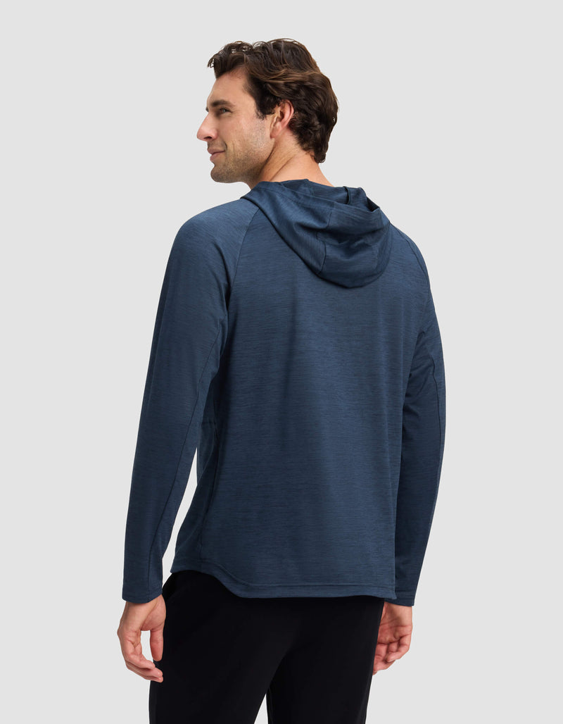 A man with short brown hair is seen from behind wearing Cozy Earth’s Men’s Lightweight Performance Hoodie in dark blue and black pants, standing against a plain light gray background.
