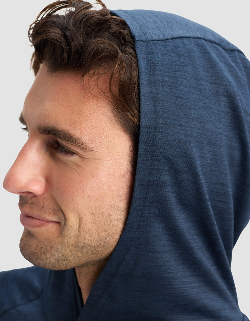 A close-up side view of a man with short brown hair wearing the Cozy Earth Men's Lightweight Performance Hoodie in blue, looking ahead with a slight smile against a plain light background.