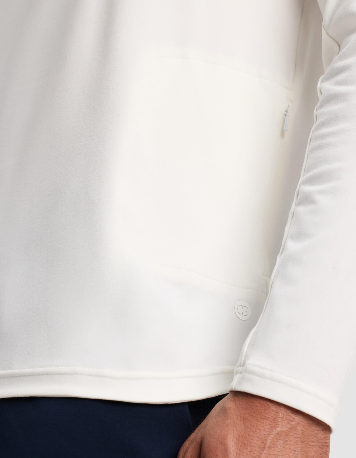 A close-up of a person wearing the Cozy Earth Men's Lightweight Performance Hoodie in white, highlighting the lower hem, a small logo detail, and part of the person's hand.