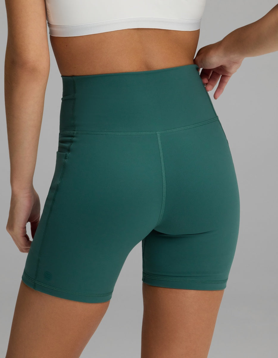 Rear view of dark green Women’s Liv Biker Short 6″ with Pockets featuring a high-waisted design and side pockets.|Color:Uniform