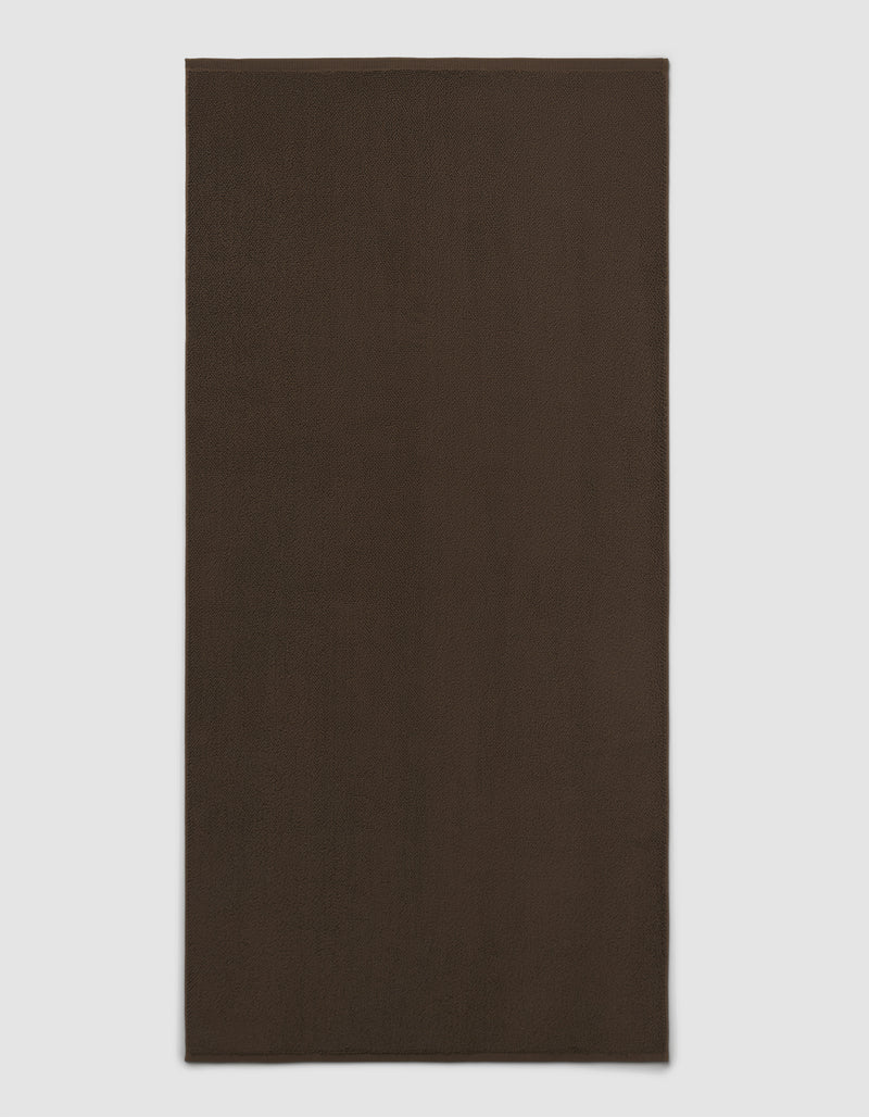 The Cozy Earth Loop Terry Bath Mat is shown on a light gray background. This plain, rectangular bath mat features a dark brown, solid color design without patterns or visible texture.