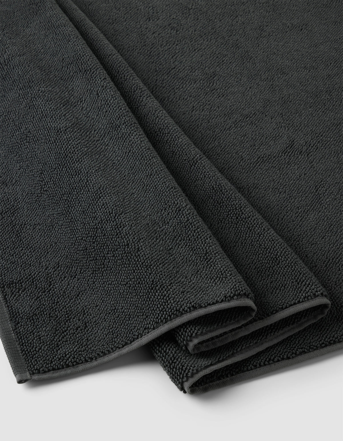 A close-up of the Cozy Earth Loop Terry Bath Mat, neatly folded in dark gray with a soft, textured surface, displayed on a light-colored background.