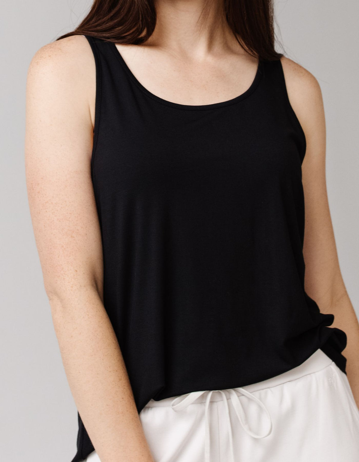 A woman wears the Cozy Earth Women's Bamboo Stretch-Knit Lounge Tank in black. She stands against a plain background, with her loose brown hair over her shoulders and face partially out of frame.