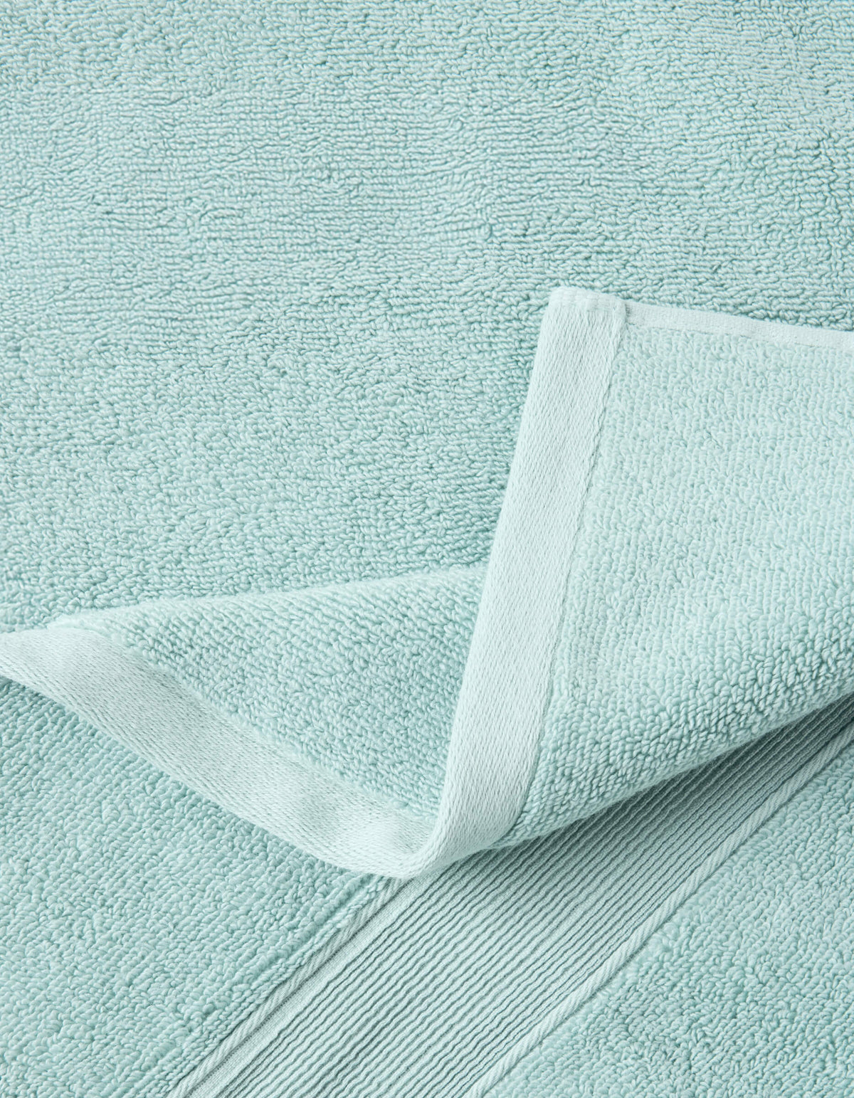 A close-up of a Luxe Bath Towel by Cozy Earth in light blue highlights its textured, soft, and absorbent fabric with detailed stitching and a neatly folded corner.