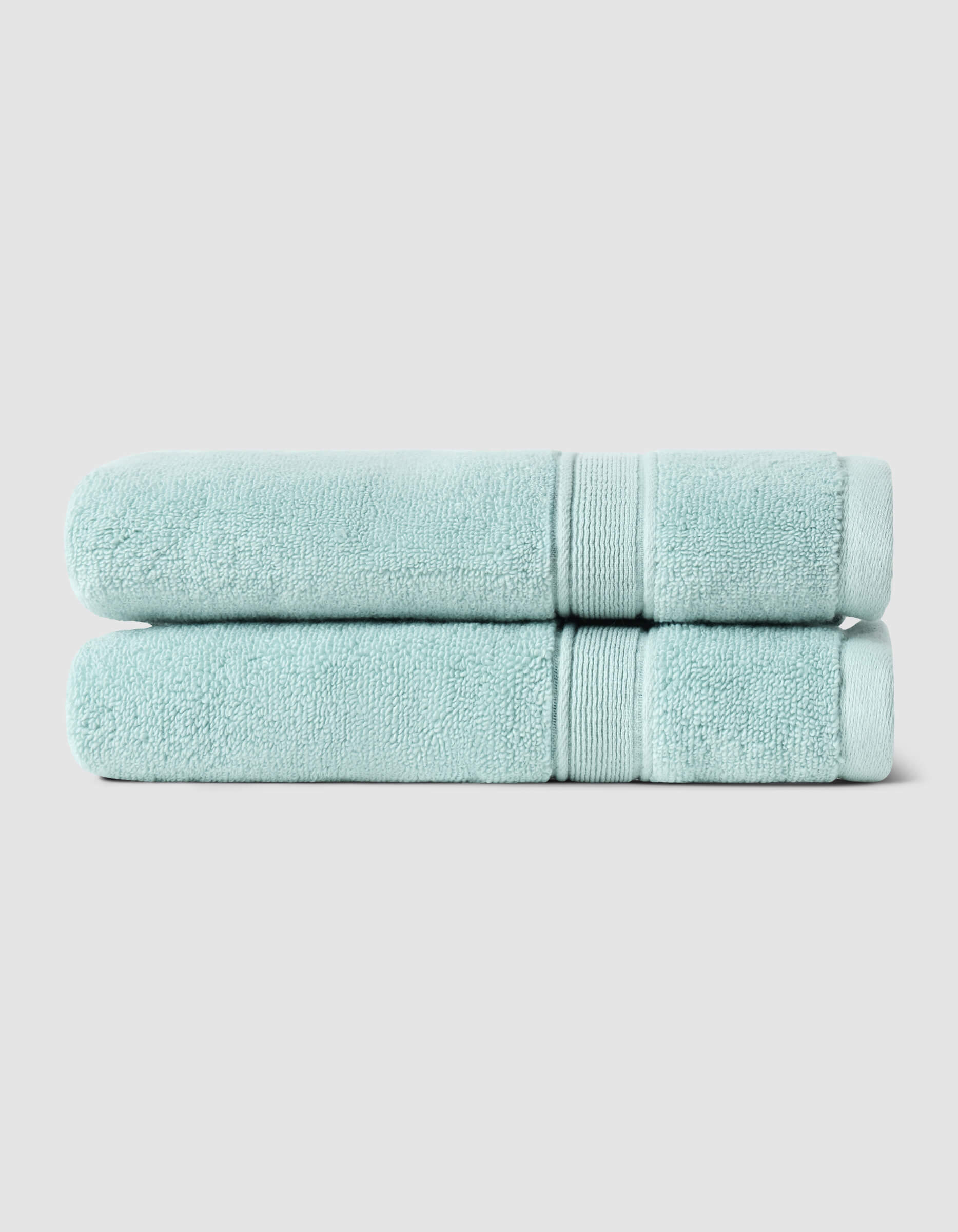 Two neatly folded Luxe Hand Towels by Cozy Earth, in light blue, are stacked atop each other against a plain light gray background.|Color:Tide