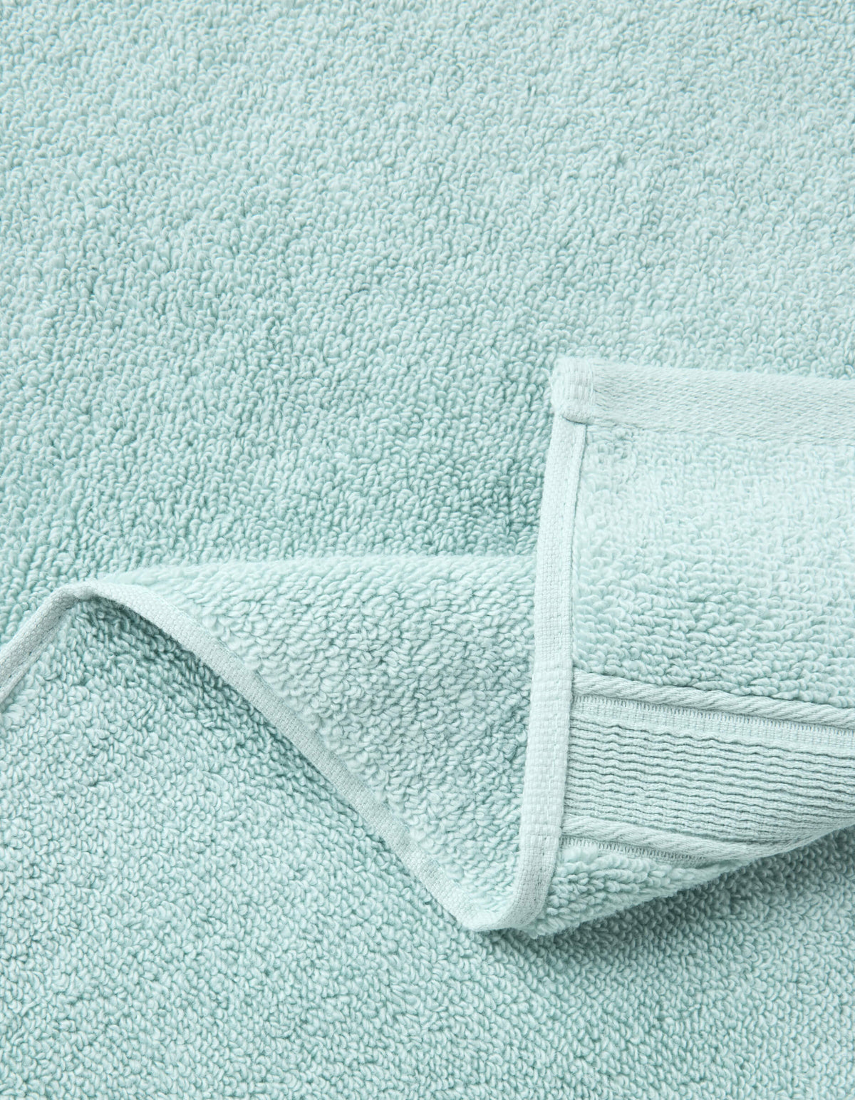 A close-up of Cozy Earth Luxe Washcloths in light blue, with one corner neatly folded to display the plush terry texture and detailed stitched edging.