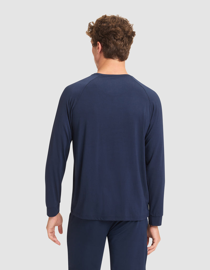 A man with short curly hair faces away from the camera, wearing Cozy Earth's Men's Bamboo Stretch-Knit Long Sleeve in navy blue, paired with matching pants, against a light gray background.