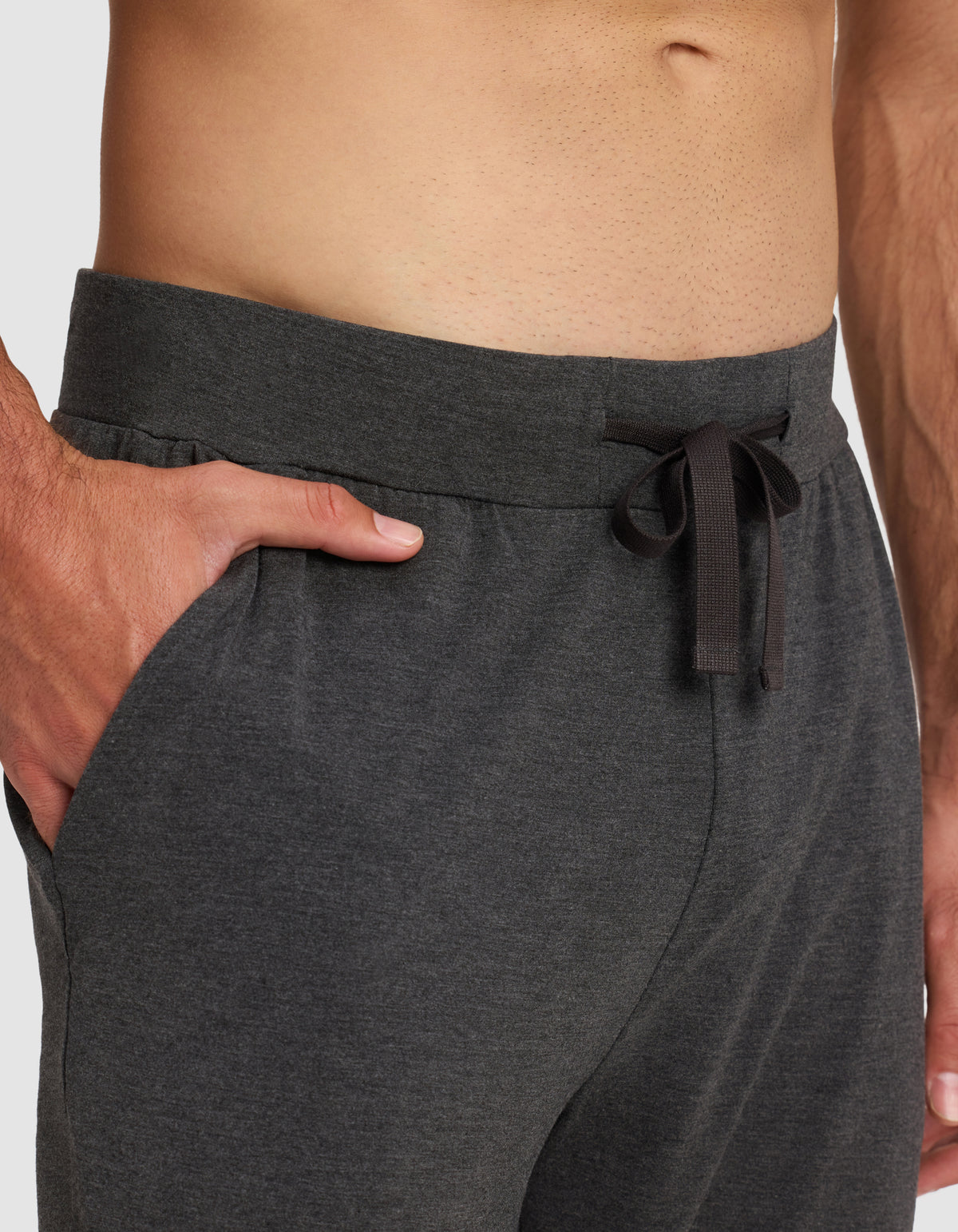 A close-up of a person wearing Cozy Earth Men's Bamboo Stretch-Knit Pajama Pants in dark gray, featuring a drawstring waistband and pockets; their bare torso is visible above the waistline.