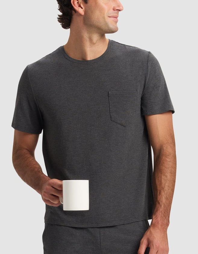 Man wearing a dark gray t-shirt and shorts holding a white mug on a light gray background