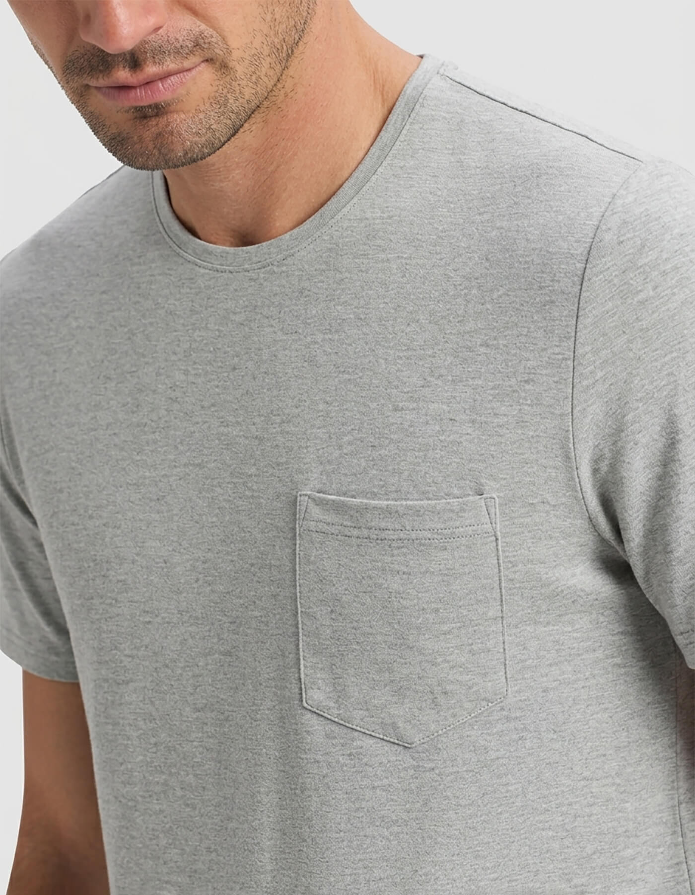 A man is shown from shoulders to mid-torso, facing slightly sideways, wearing the Cozy Earth Men's Bamboo Stretch-Knit Short Sleeve Pajama Set in light gray with a chest pocket against a plain background.|Color:Heather Grey