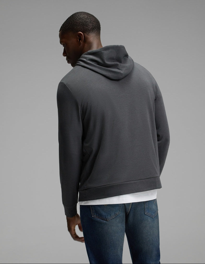 A man wearing the Cozy Earth Men’s Brushed Bamboo Hoodie in dark gray and blue jeans stands with his back to the camera against a plain gray background.|Color:Charcoal
