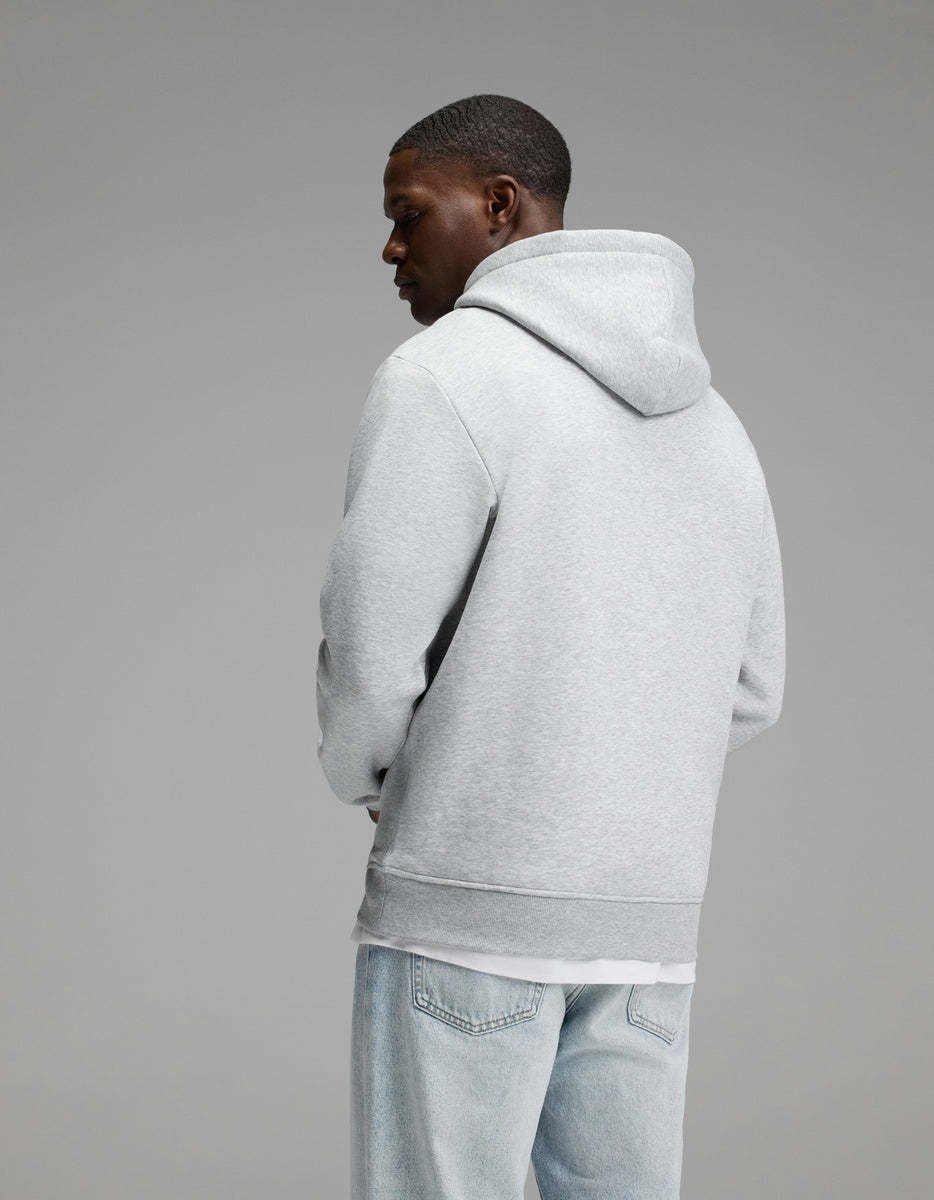 A person wearing the Cozy Earth Men’s Cityscape Hoodie in light gray and light blue jeans stands facing away from the camera against a plain gray background.|Color:Heather Grey