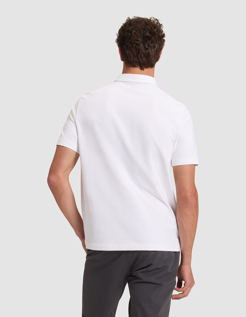 A man is seen from behind wearing the Cozy Earth Men's Everyday Polo in white with dark gray pants, standing against a light gray background.