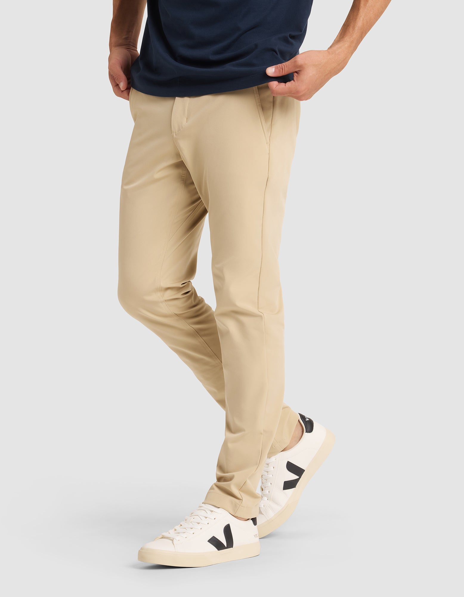 A person wearing Cozy Earth's Men's Everywhere Pant in beige, paired with a dark navy shirt and white sneakers with black "V" logos, stands hands-in-pockets against a plain light background. Only the lower half of the body is shown. |Color:Khaki