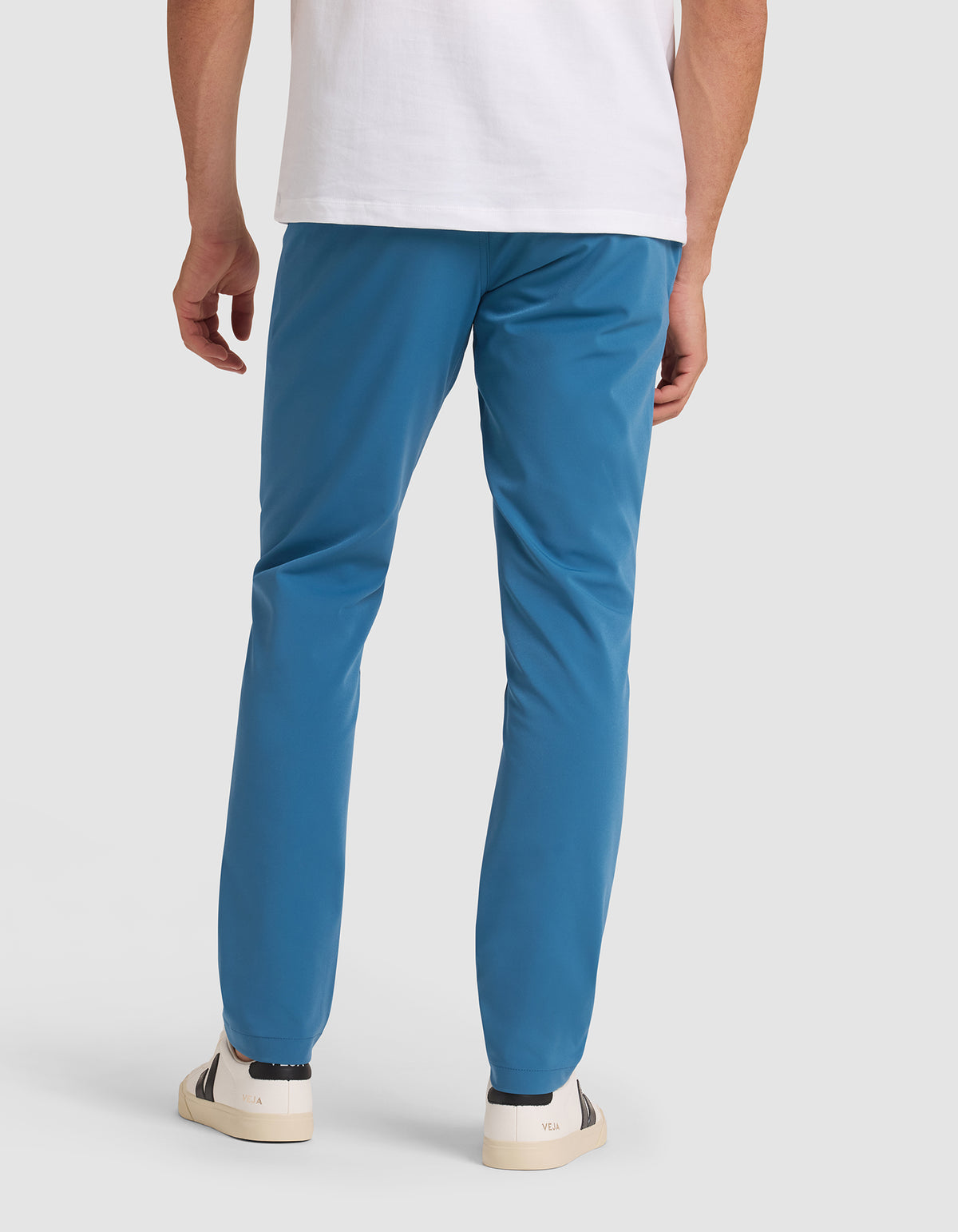 A person models the back view of the Cozy Earth Men's Everywhere Pant, paired with a white t-shirt and white sneakers with dark accents, against a plain light background.  