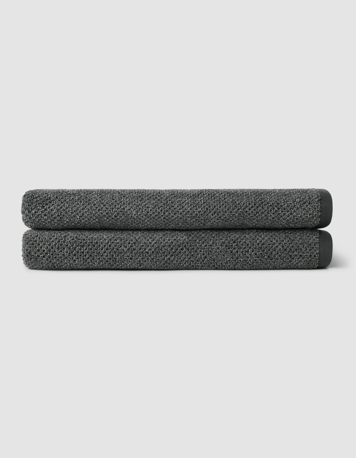 Two neatly folded Cozy Earth Nantucket Bath Sheets in dark gray are stacked on top of each other against a plain light gray background.|Color:Graphite