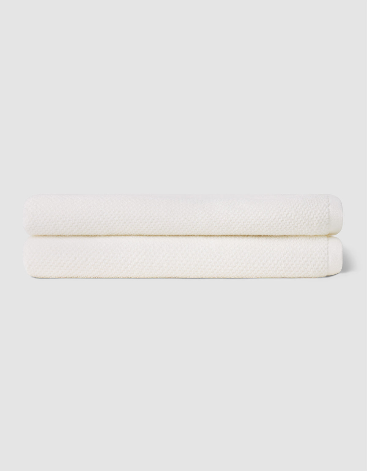 Two neatly folded Cozy Earth Nantucket Bath Sheets are stacked atop each other against a plain, light-colored background.|Color:White