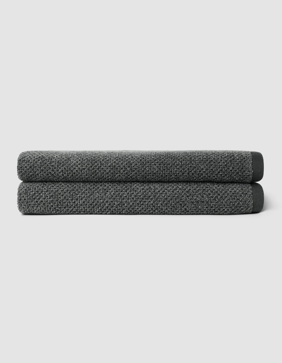 Two neatly folded Nantucket Bath Towels by Cozy Earth, in dark gray, are stacked atop one another against a plain light gray background.