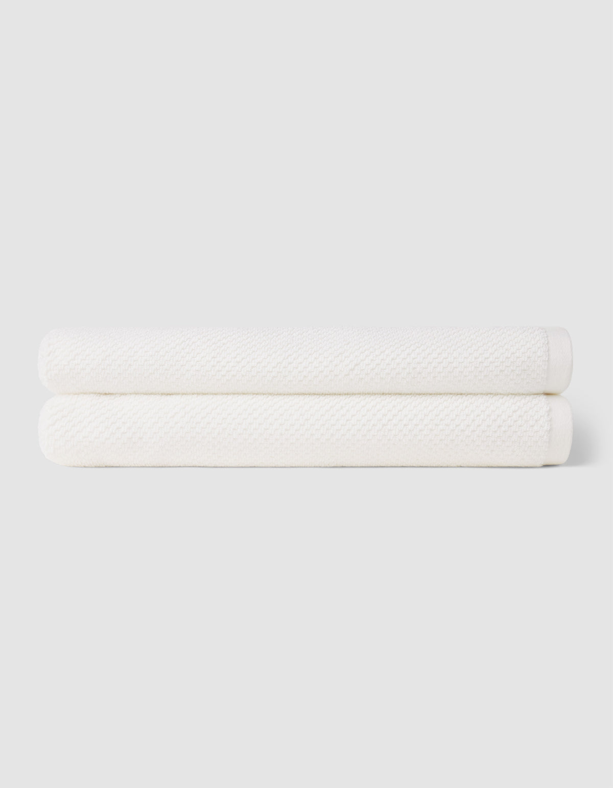 Two neatly folded Nantucket Bath Towels by Cozy Earth are stacked together against a plain light gray background.