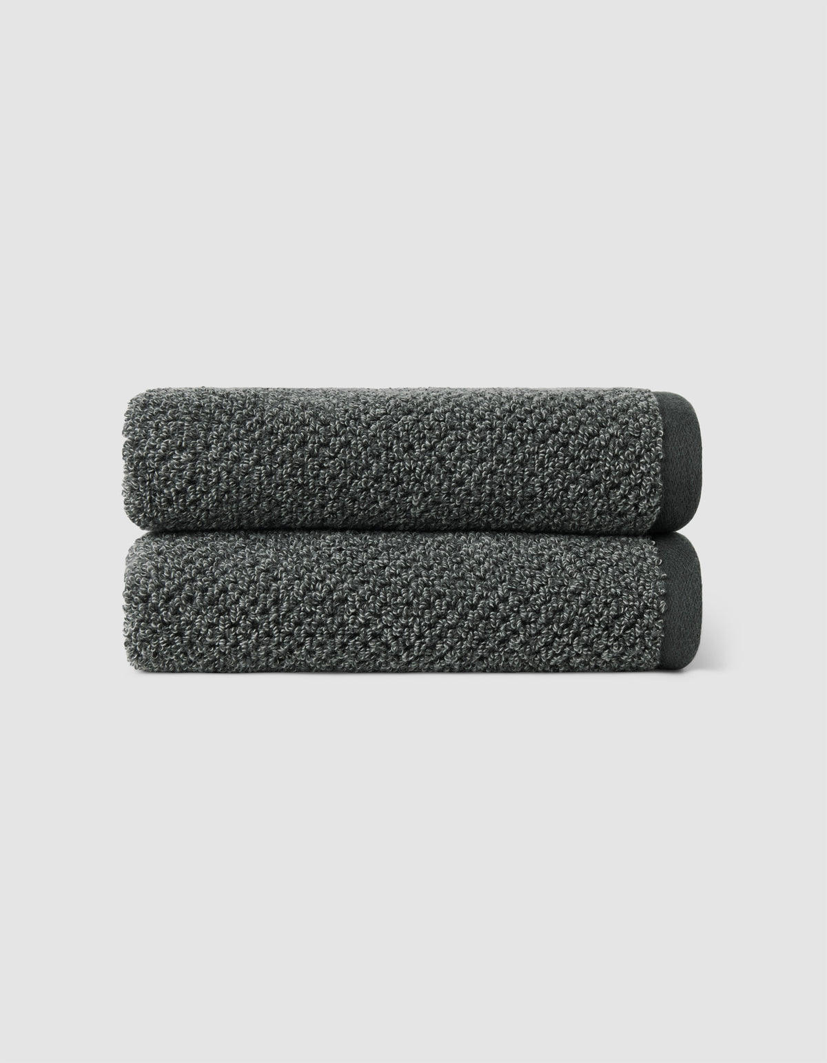 Two dark gray Nantucket Hand Towels by Cozy Earth, neatly rolled and stacked, set against a plain light gray background.|Color:Graphite