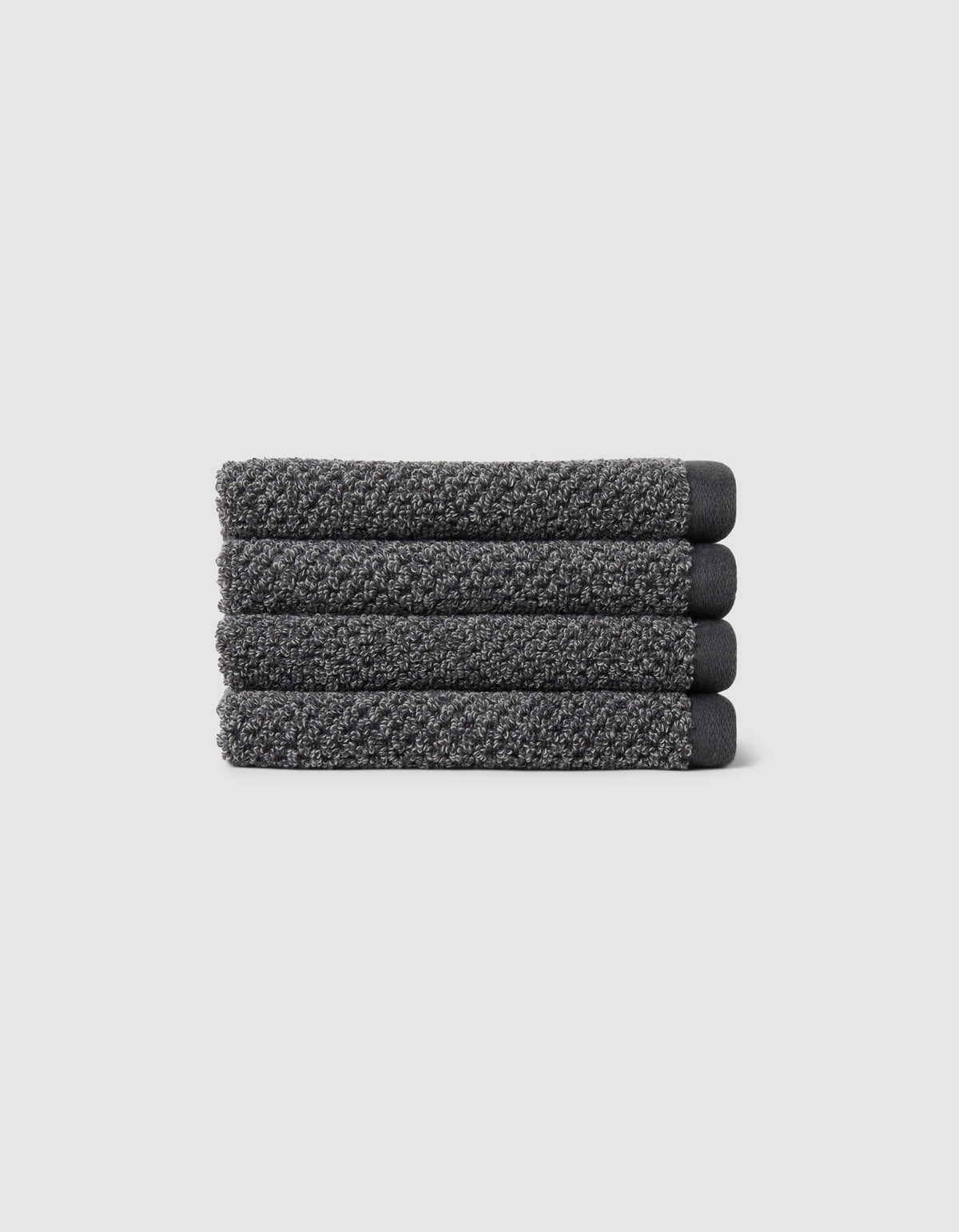Four neatly folded Nantucket Washcloths by Cozy Earth, textured in dark gray, are stacked horizontally on a plain light gray background.|Color:Graphite