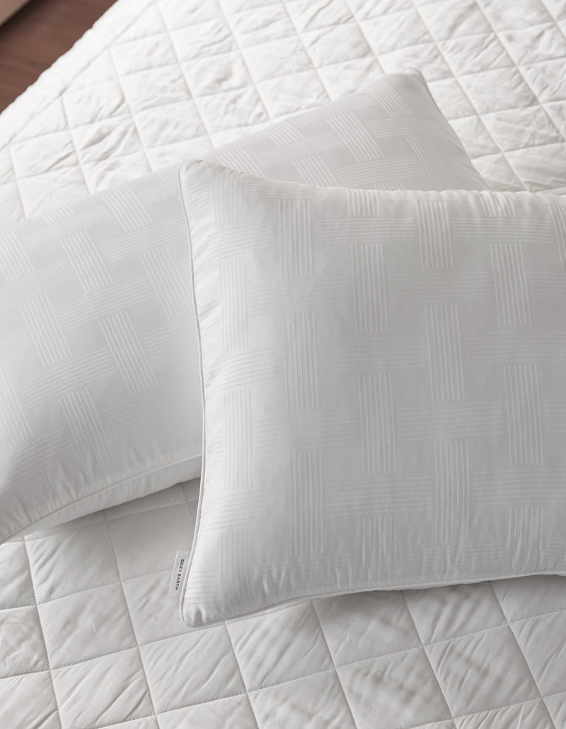 Two Cozy Earth Pillow Protectors in white, featuring a subtle geometric pattern, rest on a matching quilted bedspread. The bedding looks clean, crisp, and neatly arranged.