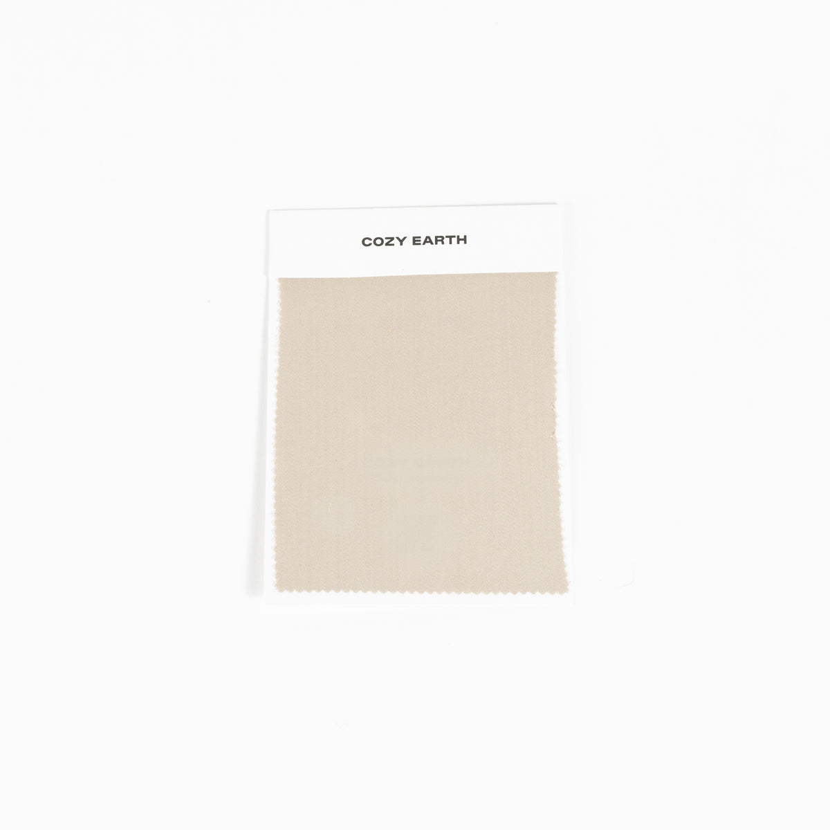 A square fabric sample from Cozy Earth, identified as the Bamboo Sheet Swatch. The swatch is a simple beige color with a zigzag edge design and is attached to a white card. 