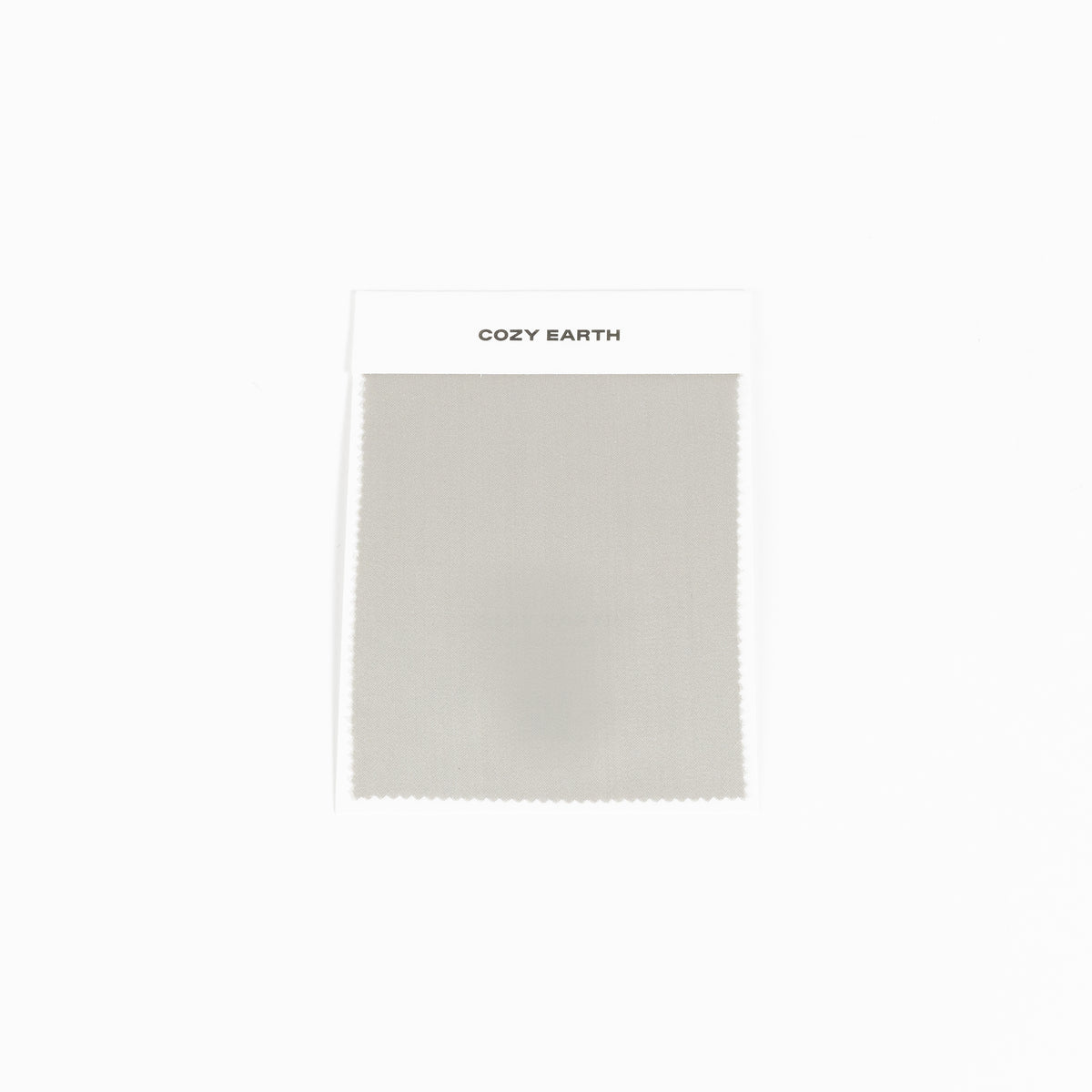 A "Bamboo Sheet Swatch" from Cozy Earth, featuring a light gray fabric with a smooth texture and a zigzag edge, displayed against a white background. 