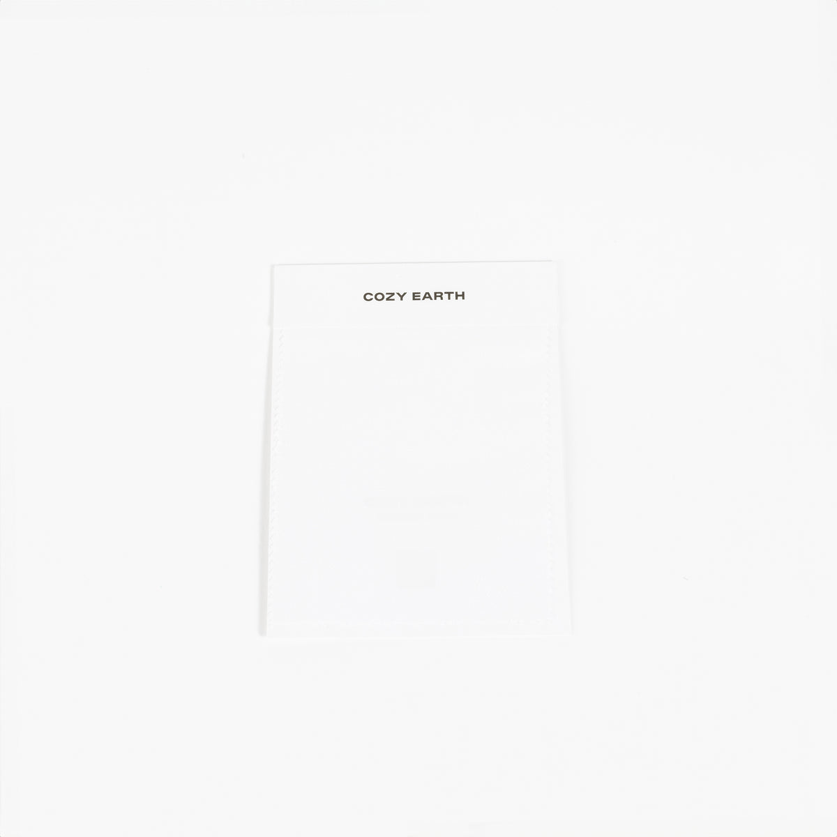 A white fabric label prominently displays the brand name "Cozy Earth" at the top, set against a plain white background to highlight its minimalist design. 